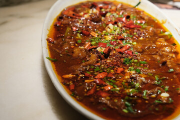 close up Poached Sliced Beef in Hot Chili Oil in plate on table. traditional Chinese Sichuan Cuisine. blur background