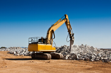 The breaker used to break up boulders in an open cast mine. Large yellow machinery crushing spodumene ore in a lithium mine.