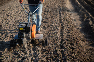 small orange plowing machine in hands of a farmer making arable in black soil