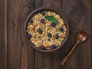 Top view of a clay bowl with granola and a wooden spoon on a wooden table.