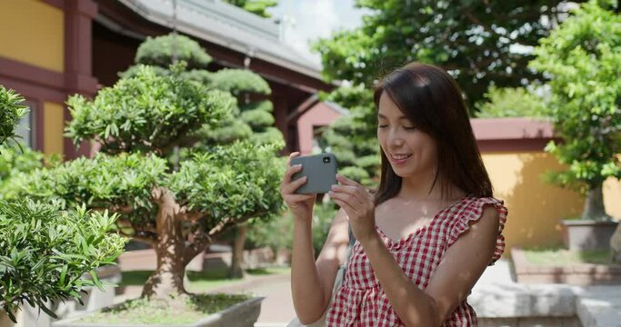 Woman use of mobile phone to take photo in chinese garden
