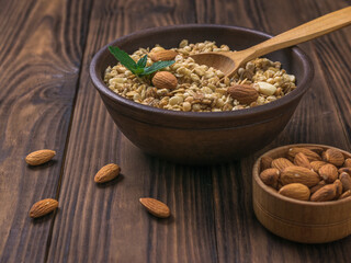A wooden bowl with almonds and a clay bowl with granola on a wooden table.