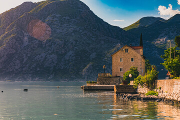 Fototapeta premium Old stone house in Kotor Bay with mountains and crystal clear water in the Balkans, Montenegro on the on Adriatic Sea