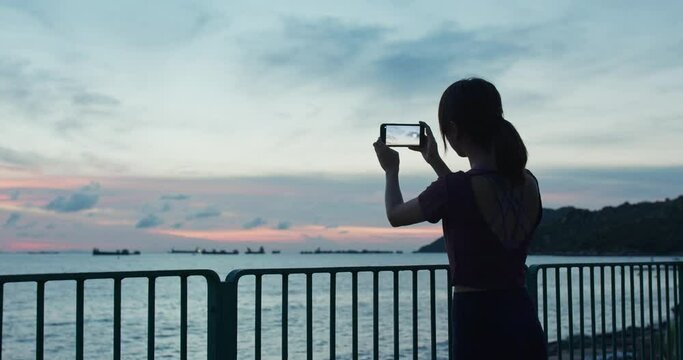 Woman use of mobile photo take photo at sunset time beside the sea