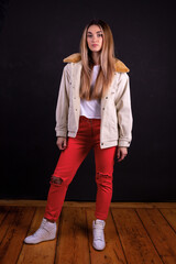A young girl in a jacket and red trousers isolated on a black background
