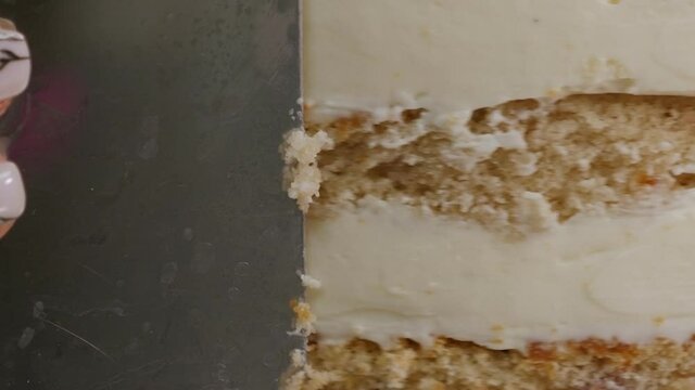 Close-up of a pastry chef using a metal spatula aligns the top and sides of a cake in a pastry shop. The pastry chef levels the cake with a spatula, the cake is on a turntable.
