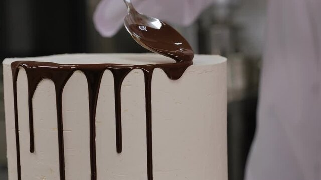 Close-up of a pastry chef pouring liquid chocolate on a white cream cake. The process of making a creamy cake with chocolate drips. The process of decorating the cake with liquid chocolate.