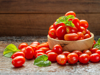 Small red fresh tomatos in wood bowl on wood table with nature light.