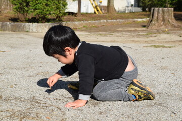 公園の地面に絵を描いて遊ぶ3歳の男の子

