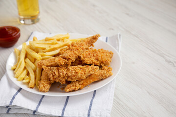 Homemade Crispy Chicken Tenders and French Fries with sauce and glass of cold beer, side view. Copy space.