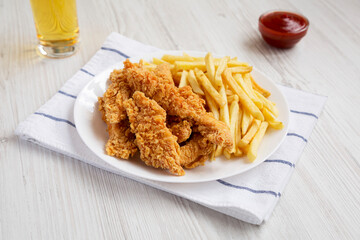 Homemade Crispy Chicken Tenders and French Fries with sauce and glass of cold beer, side view.