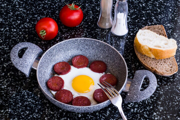 Egg with sausage in egg pan on granite marble table with a fork,top view and flat layout.