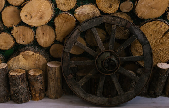 A wooden wheel stands near a wall of logs. The old wheel.