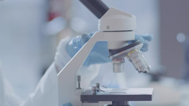 A female scientist using a pipette in a professional laboratory and researching a blood sample with a microscope. We can see her male colleague in the background.