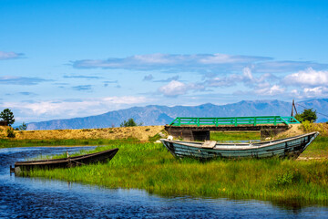 Obraz premium old boats on the banks of the river flowing into Lake Baikal, against the background of mountains and blue sky