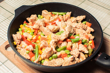 Fried tender chicken pieces with vegetable mixture in pan on wooden board.