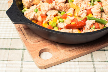 Fried tender chicken pieces with vegetable mixture in pan on wooden board.