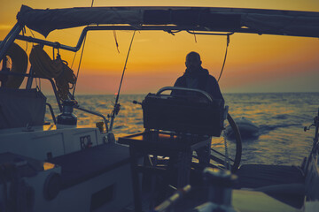 Sailor steering sailing boat with a rudder in dawn / twilight time on tje open sea. © astrosystem