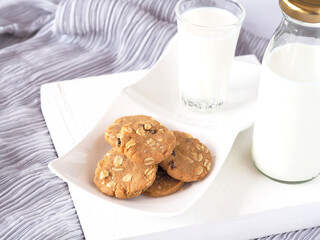 A pile of Healthy homemade oat cookies with milk on a white plate over grey fabric background. .