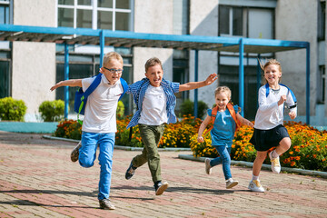group of school children with backpacks run out of school, after the end of classes. Classmates, school friends. The beginning of holidays. The end of quarantine. Back to school.