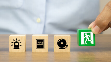 Close-up hand choose a wooden toy blocks stacked with fire exit icon for fire safety protection...