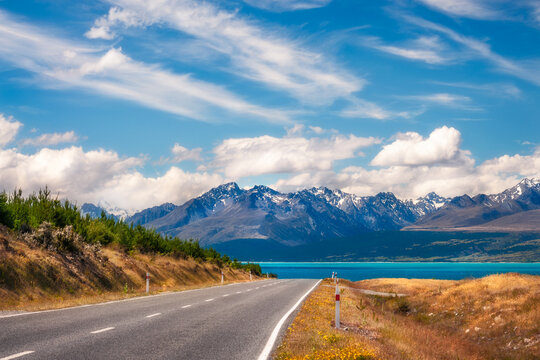 Mount Cook State Highway in New Zealand's South Island is one of the most picturesque alpine roads in the world. Winding road perspective with lake Pukaki and snow-capped mountains in the background.