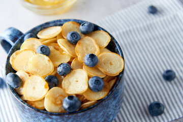 Blue Bowl of mini pancake cereal with blueberries, maple syrup and milk on concrete background. Tiny pancakes, new food trend concept. Cute healthy breakfast or snack. Recipe, menu.