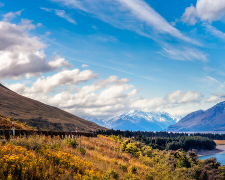 Mount Cook Highway along the shore of Lake Pukaki, in New Zealand, South Island on a beautiful summer day with snow-capped Mount Cook engulfed in clouds in the background.