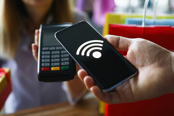 Male hand hold telephone with wireless network. Woman give cash register terminal to pay for goods using network. Man pay for goods in store using program on phone. Contactless payment system using