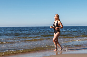 Fototapeta na wymiar young blonde girl in a black swimsuit runs along the sand of the sea shore