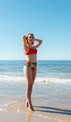 young blonde girl in a red swimsuit stands on the seashore