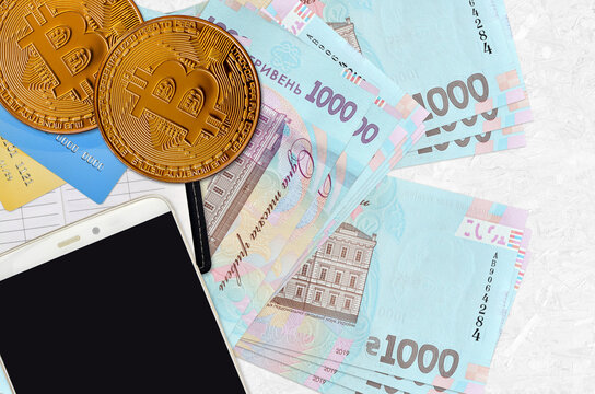 1000 Ukrainian hryvnias bills and golden bitcoins with smartphone and credit cards. Cryptocurrency investment concept. Crypto mining or trading
