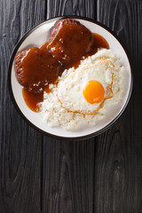 Loco Moco is Hawaiian comfort food made with rice and a burger smothered with rich gravy and egg close-up on a plate. Vertical top view