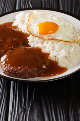 Loco Moco is Hawaiian comfort food made with rice and a burger smothered with rich gravy and egg close-up on a plate. Vertical