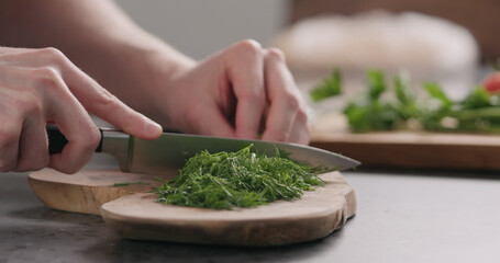 man chopping fresh dill on olive board side view