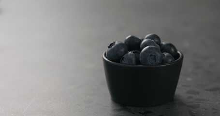 small black bowl with fresh blueberries on concrete surface with copy space