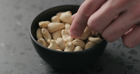 man hand takes cashew nuts from black bowl on terrazzo countertop