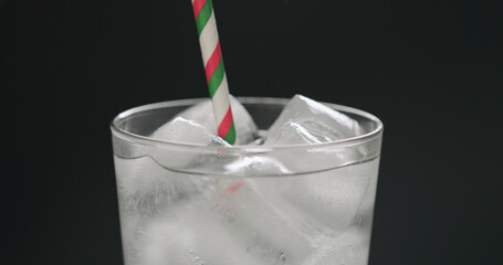 drink with paper straw soda from glass with ice cubes on black background closeup