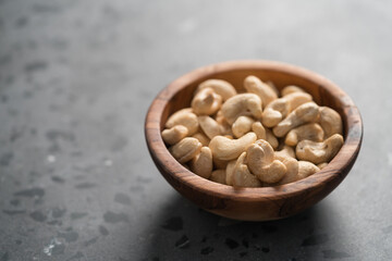 Dry cashew nuts in wood olive bowl on concrete background with copy space