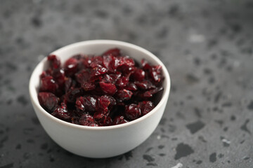 Dried cranberries in white bowl on concrete surface