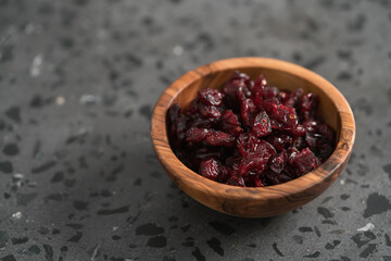 Dried cranberries in olive wood bowl on concrete surface