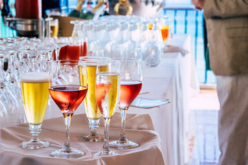Close up og glasses with coloured fresh tasty drinks with alcohol and not on a table during catering party event - restaurant and people in defocused background