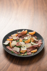 Salad with prosciutto, tangerines and vintage cheese on walnut table with copy space