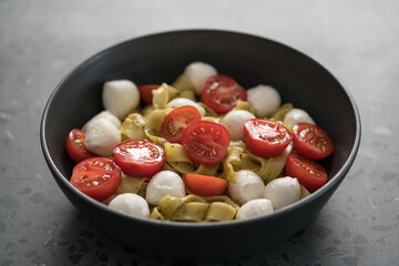 fettuccine pasta with pesto, mozzarella and cherry tomatoes in black bowl on concrete background