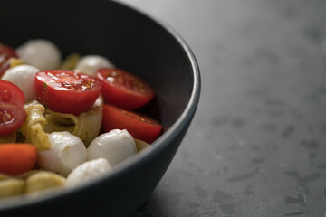 fettuccine pasta with pesto, mozzarella and cherry tomatoes in black bowl on concrete background closeup with copy space