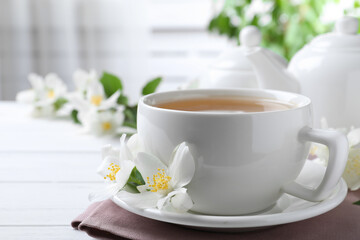 Obraz na płótnie Canvas Cup of tea and fresh jasmine flowers on white wooden table
