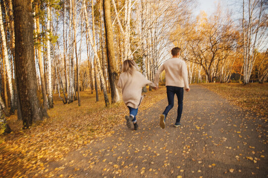 Happy couple in love runs through autumn forest, man smile throws maple yellow leaves