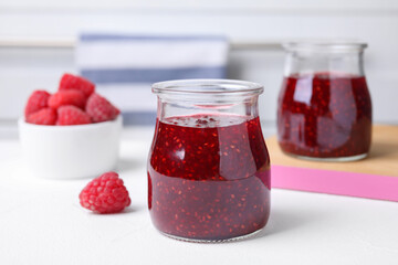 Delicious jam and fresh raspberries on white table, closeup