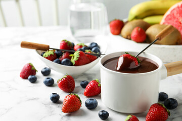 Fondue pot with chocolate and fresh berries on white marble table