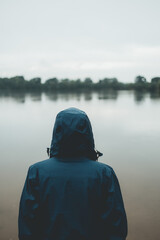 Person in einer Regenjacke schaut auf einen See bei trübem Regenwetter